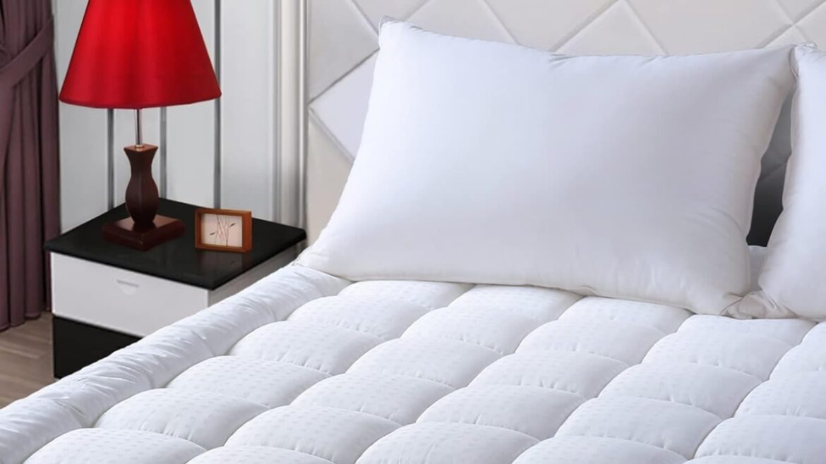 White quilted mattress topper on a neatly made bed with two pillows and a bedside lamp.