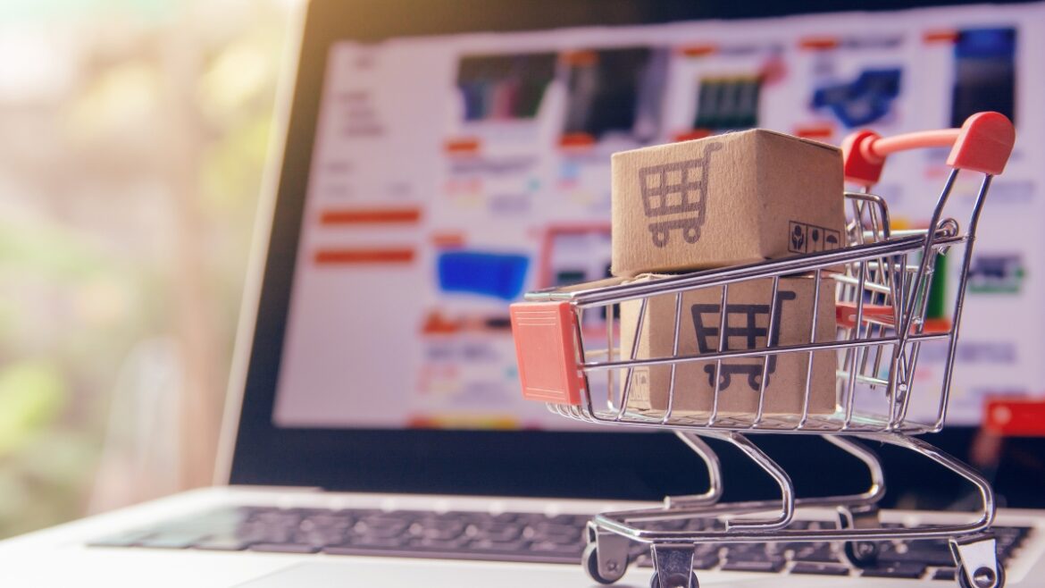 Small shopping cart with boxes in front of a laptop showing an online store.
