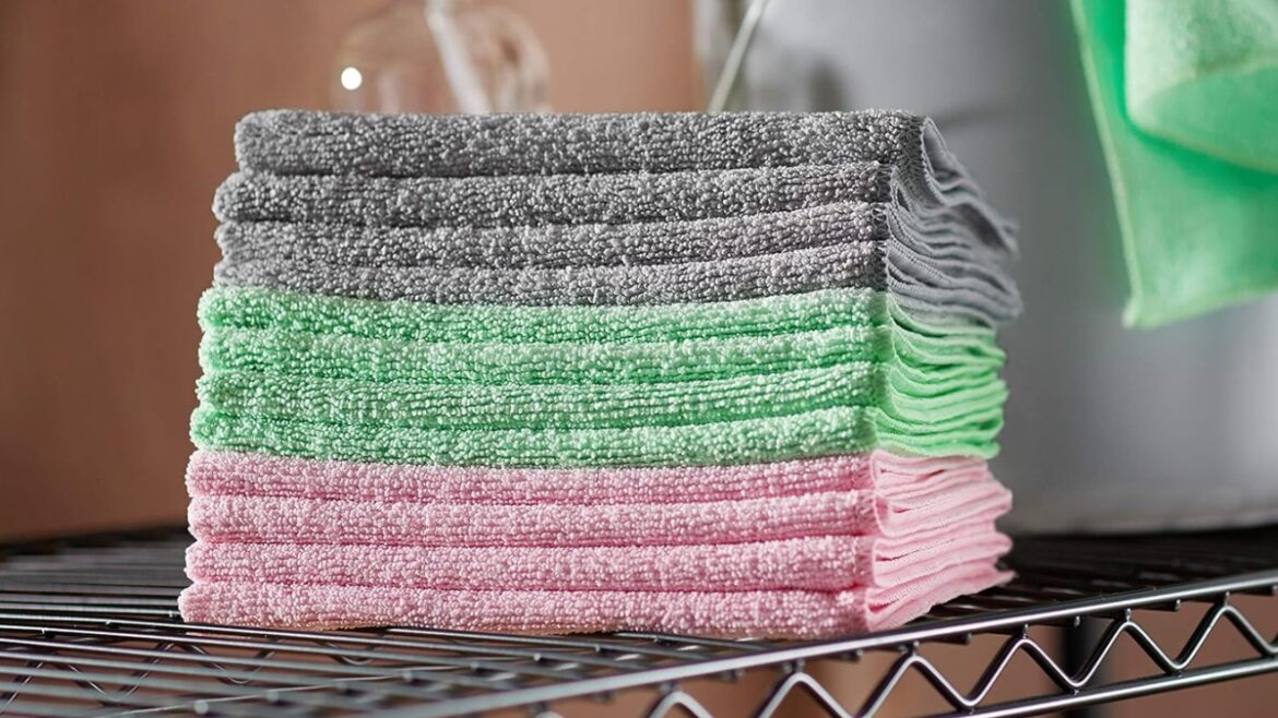 Stacked Amazon Basics microfiber cleaning cloths in gray, green, and pink on a metal shelf.