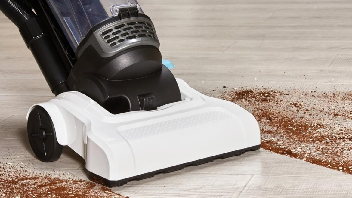 Amazon Basics vacuum cleaner picking up dirt on a hard floor with a wide suction path and large dust cup.