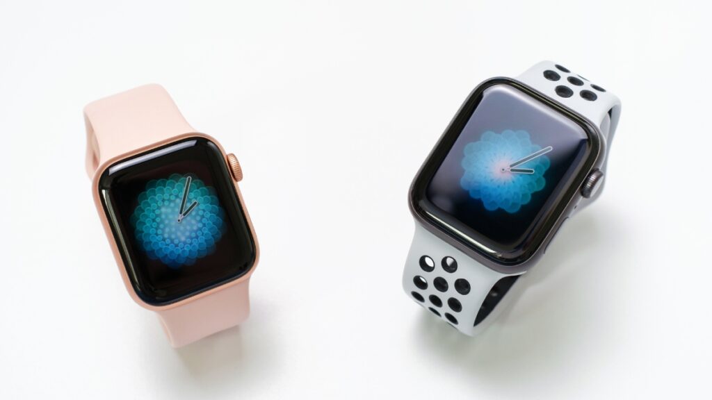 Two smartwatches with digital flower displays on white background, one with a pink band and the other with a white and black perforated strap.