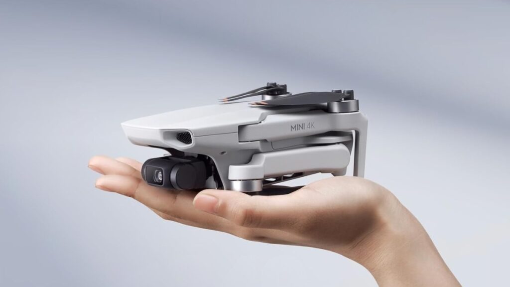 Folded DJI Mini 4K drone resting on an open hand, showing its compact and lightweight design against a soft gray background.